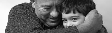 Photo en noir et blanc montrant un grand-père enlaçant son petit-fils en plan rapproché.