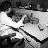Une femme portant un sarrau est assise à un bureau dans un laboratoire et manipule un appareil.