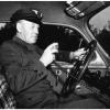 Photographie en noir et blanc montrant un chauffeur de taxi assis dans son véhicule. 