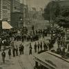 Photo ancienne d'une foule sur une place lors d'un défilé où on aperçoit un tramway.