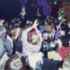 Photo couleur d’un spectacle à l’intérieur d’un bar. Une chanteuse se trouve à l’avant, et devant elle, des femmes assises à des tables applaudissent. 