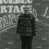 Un homme pose devant une murale où on peut lire le slogan « Un Québec de partage, ça s’impose. 1 mai 1996 ».