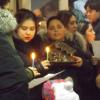Groupe de personnes de différents âges pour une célébration de Noël. Quelques-uns tiennent des bougies, un tient une crèche. 