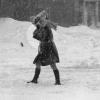 Une jeune femme tente de se protéger du vent et de la neige coiffée d’un journal
