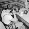 Un homme en tenue décontractée est assis derrière un bureau sur lequel il y a trois téléphones. L’homme utilise celui du centre.
