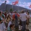 Une foule de personnes bavardent et jouent de la musique devant une pyramide du village olympique