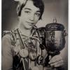 Photo noir et blanc d’une athlète de 16 ans en format taille avec plusieurs médailles autour du cou et un trophée qu’elle tient dans ses mains. 
