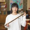 Photo d'une jeune fille d'origine chinoise tenant un objet de forme longue en bois dans une classe. L'arrière-plan est flou. 