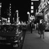 Scène de rue en soirée, avec les néons, des gens qui se promènent et des voitures