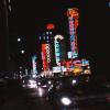 Photo couleur de la rue Sainte-Catherine la nuit avec des enseignes au néon et des voitures au premier plan. 