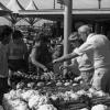 Des gens pointent des légumes autour d'un étal au marché.