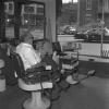 Un homme est assis à l’intérieur du salon de coiffure Barbier A. Plouffe et regarde à l’extérieur par la grande fenêtre.