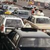 Photo couleur montrant plusieurs taxis de différentes compagnies dans un stationnement. Quelques hommes sont regroupés près d’une des voitures. 