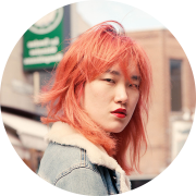 Photo couleur mi-corps d'une jeune fille d'origine chinoise à la chevelure flamboyante qui prend la pause dans une rue animée.