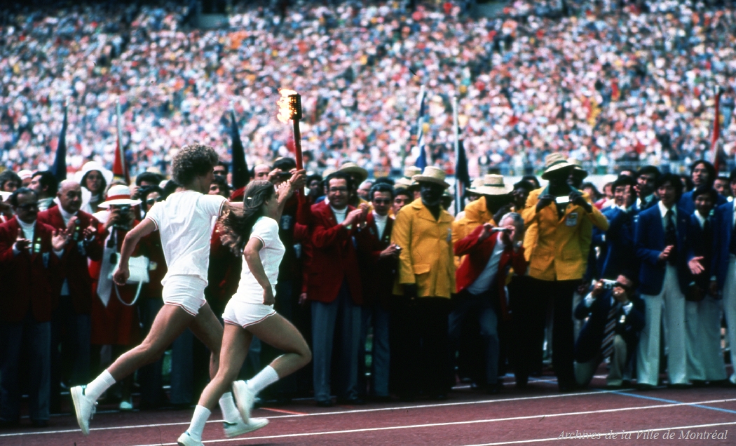 Deux athlètes courent en tenant la flamme olympique à la cérémonie d’ouverture des Jeux olympiques de 1976.