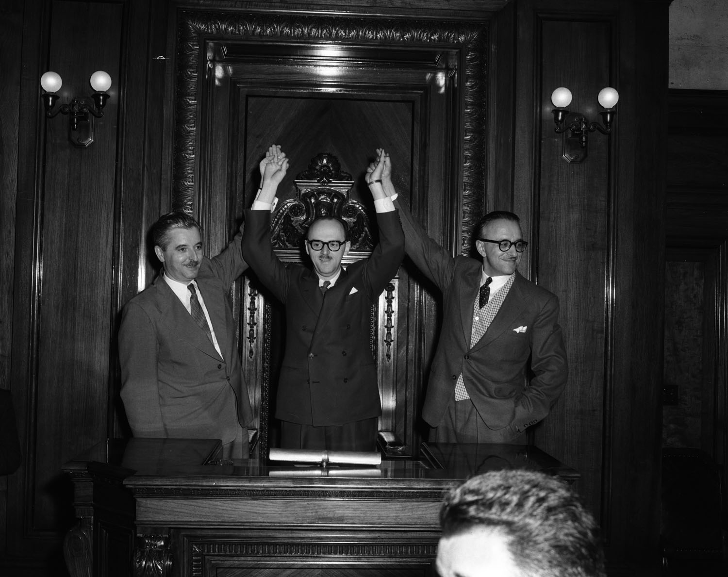 Photo noir et blanc montrant trois hommes les bras en l'air en signe de victoire.
