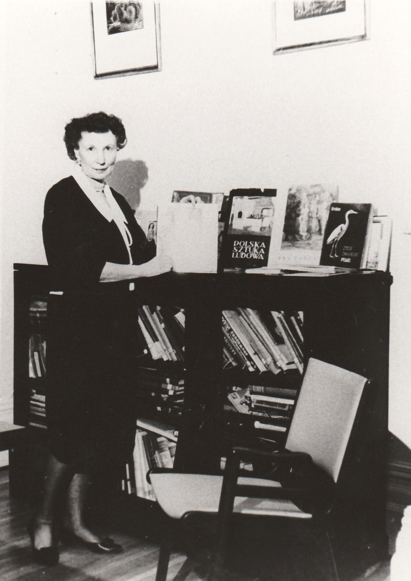 Wanda Stachiewicz tenant un livre, une bibliothèque derrière elle