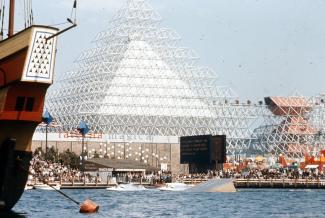 Vue extérieure du lac des Dauphins et de l’attraction nommée Gyrotron de l’Expo 67, avec sa pyramide blanche et le volcan à droite de la photographie. Le Minirail rejoignant les deux structures est également visible.