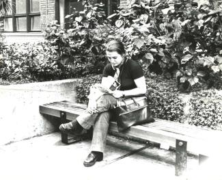 Photo noir et blanc d’une jeune femme lisant, assise sur un banc à l’extérieur d’un édifice.