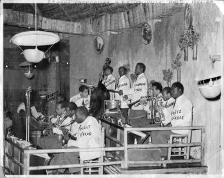 Joe Trouillot est debout entre deux rangées de musiciens dans un cabaret en Haïti.