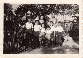 Photo en noir et blanc d’une famille de sept enfants avec la mère et le père. La mère tient le plus jeune dans ses bras.