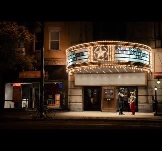 Devanture du Rialto de nuit. Deux personnes sont en discussion devant l'entrée.