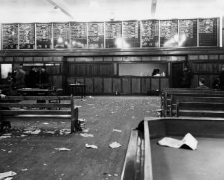 Intérieur d’une salle de paris. Des bancs sont visibles des deux côtés de la pièce et font face à un comptoir de paris. Des papiers jonchent le sol.