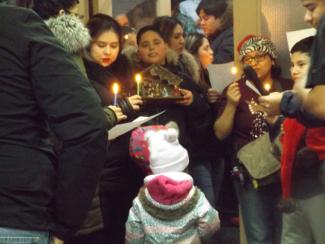 Groupe de personnes de différents âges pour une célébration de Noël. Quelques-uns tiennent des bougies, un tient une crèche.