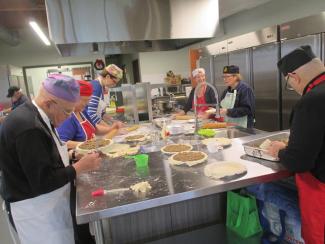 Six hommes et femmes préparent des pâtés à la viande dans une cuisine