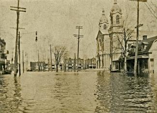 Une place inondée, entourée de maisons et d’une église.