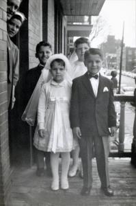 Quatre enfants habillés pour leur communion sur un balcon au 3e étage d’un triplex. Les parents sont à la porte.