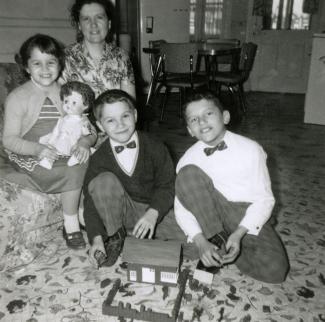 Une mère et ses trois enfants prennent la pose avec les cadeaux de Noël reçus dans leur salon. On voit la cuisine à l’arrière-plan.