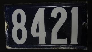 Photographie d’une plaque d’adresse rectangulaire avec les chiffres 8421 écrits en blanc sur fond bleu.