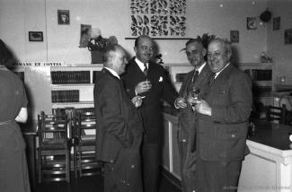 Quatre hommes verre à la main sourient dans une bibliothèque.