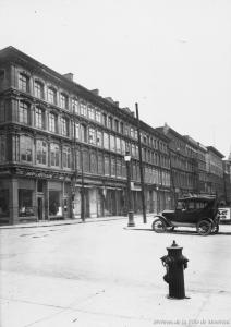 Photographie d'une enfilade de bâtiments à fenêtres le long de la rue Notre-Dame, et d'un angle de rue, vus de l'ouest.