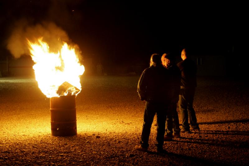 Trois individus devant un feu en plein-air.