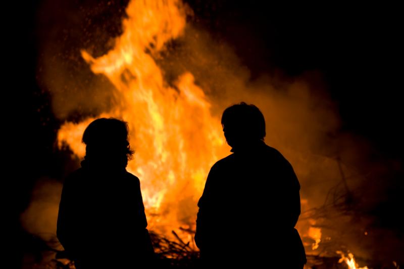 Deux individus devant un feu en plein-air.