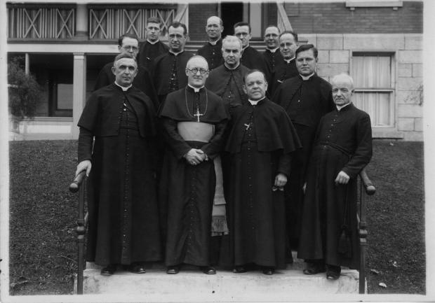 Un groupe de religieux de Sainte-Croix pose en rangées devant un édifice.