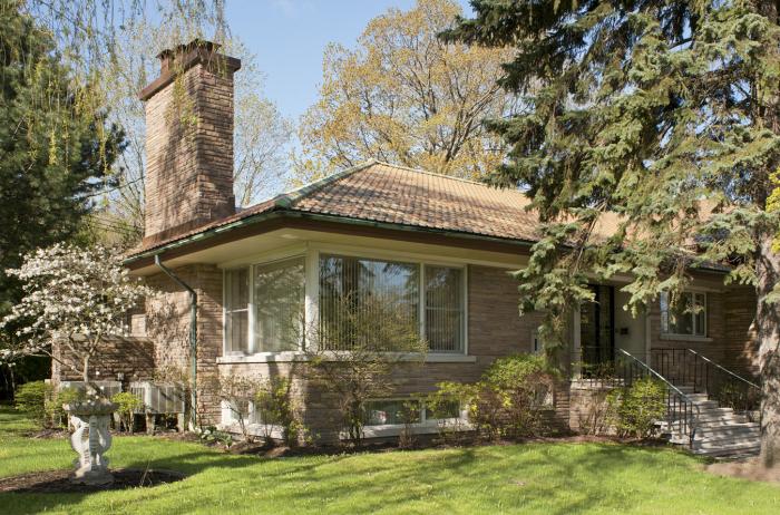 Vue d’angle de la maison E. Dossin montrant notamment le toit en croupe recouvert de tuiles d’argile et dominé par une imposante cheminée. Photographie.