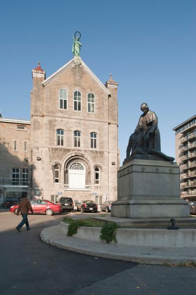 La façade monumentale de l’ancien dispensaire rappelle l’architecture des églises néo-romanes. Au centre de la cour d’honneur est érigée une statue de Jeanne Mance. Photographie.