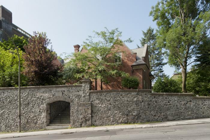 Vue du mur de soutènement de pierre gris-bleu érigé en 1912. Au-dessus de l’arc surbaissé de l’entrée se trouve l’inscription gaélique Fan-Na-Greine qui signifie « garder le soleil ». Photographie.