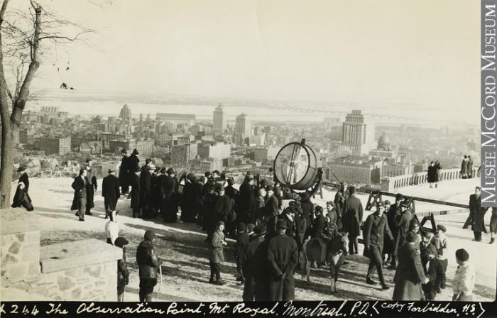 Sur le belvédère du Mont-Royal, une foule admire la vue sur le centre-ville, où on voit les gratte-ciel de l’époque, et le fleuve au loin.